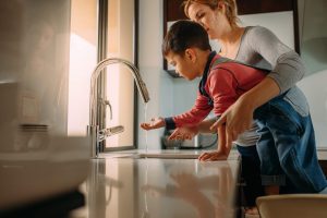 Mother helping child wash hands at kitchen sink